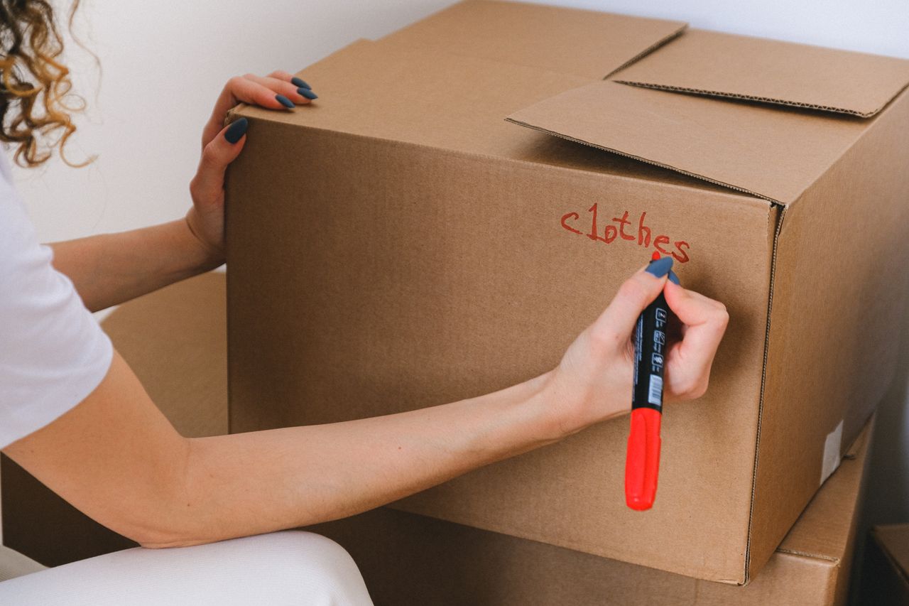 about-us Close-up of a woman labeling a cardboard box with a red marker indoors.